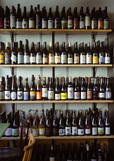 Rows of bottled drinks displayed on wooden shelves, filling the wall of a bar or speciality drinks shop.