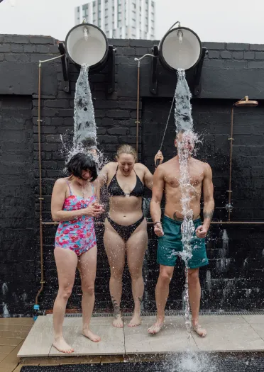 Three people in swimwear under water fountain at sauna.