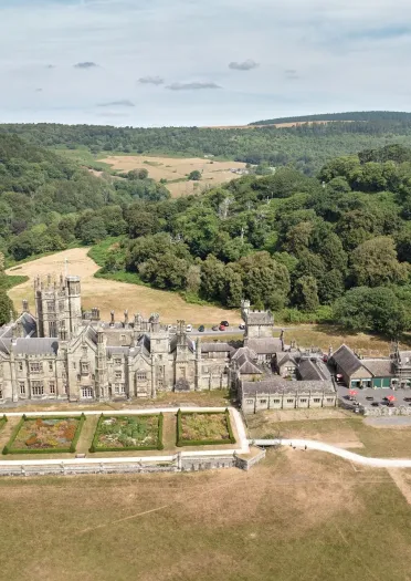 Aerial view of Margam Castle and formal gardens, surrounded by woodland and rolling countryside in Margam Park.