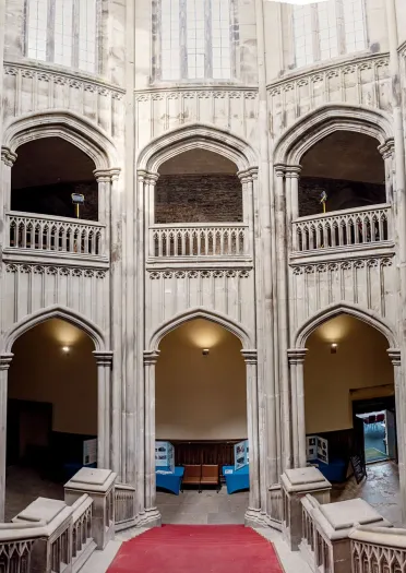 Grand stone staircase and Gothic arches inside Margam Castle's entrance hall, featuring ornate architectural details and a red carpeted stairway