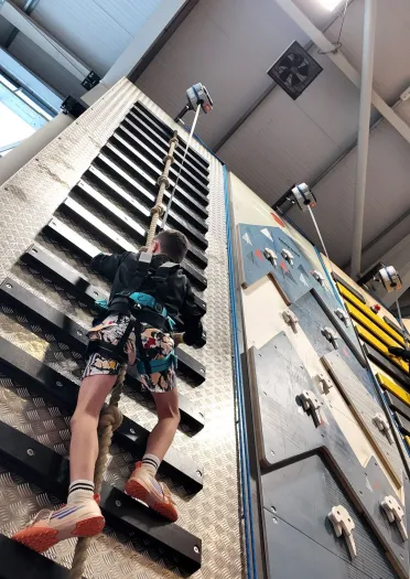 A young child in a harness on an indoor high ropes course.