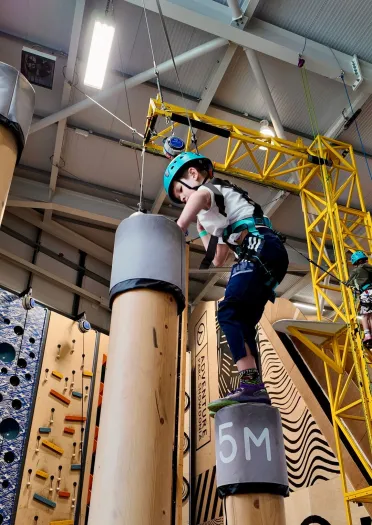 A young child in a harness on an indoor high ropes course.