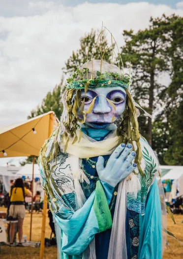 A person in a blue and green flowing costume with a mask on.