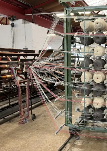 A loom for making Welsh blankets showing different colour reels of wool feeding into a loom.