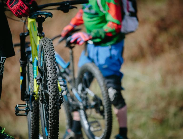 Two people in mountain biking clothing holding mountain bikes. Camera focus is on the rear wheel of one of the bikes. At Afan Forest Park, Swansea.