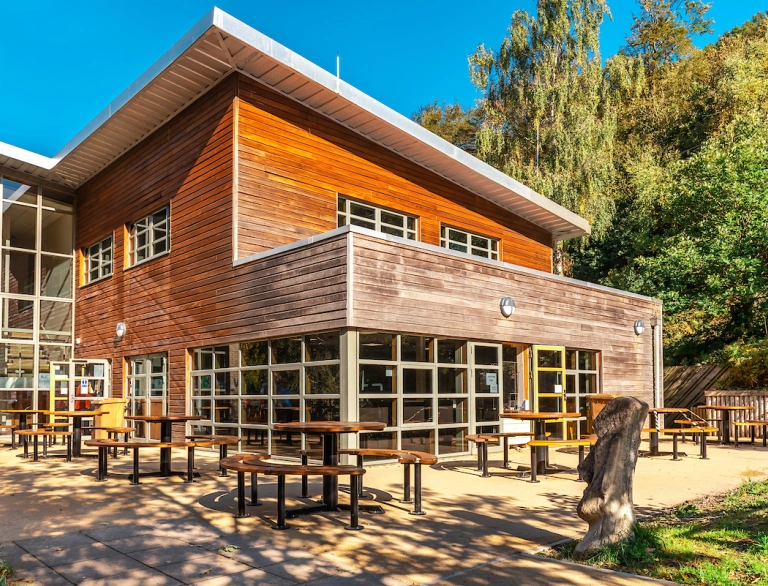 A wood panelled visitor centre surrounded by tables and seats amongst forestry.