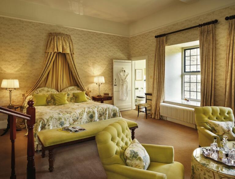A deluxe hotel room with bed, comfy chairs and en-suite bathroom.