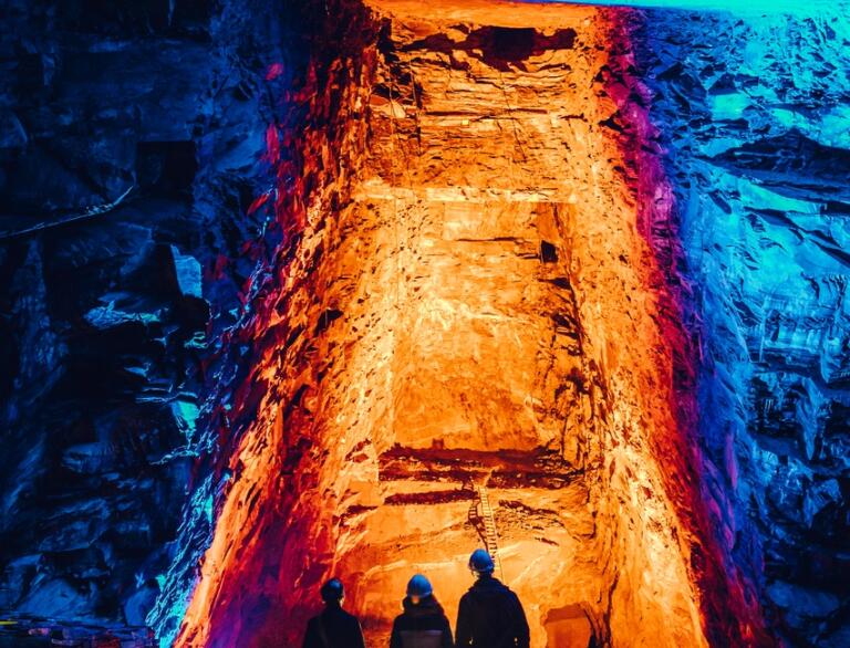 People looking at a colourfully lit underground slate cavern.