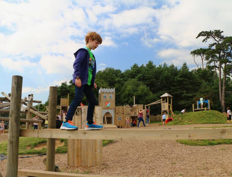 11 year old boy walking across a plank in an adventure playground