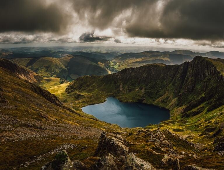 Rugged mountains surrounding a lake with dramatic clouds above.