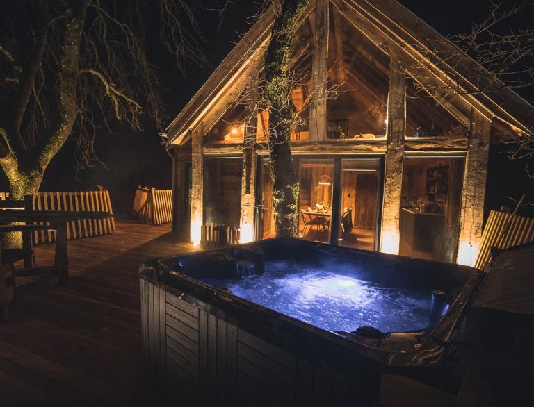 Bubbling hot tub lit from below on a deck outside a luxury treehouse.
