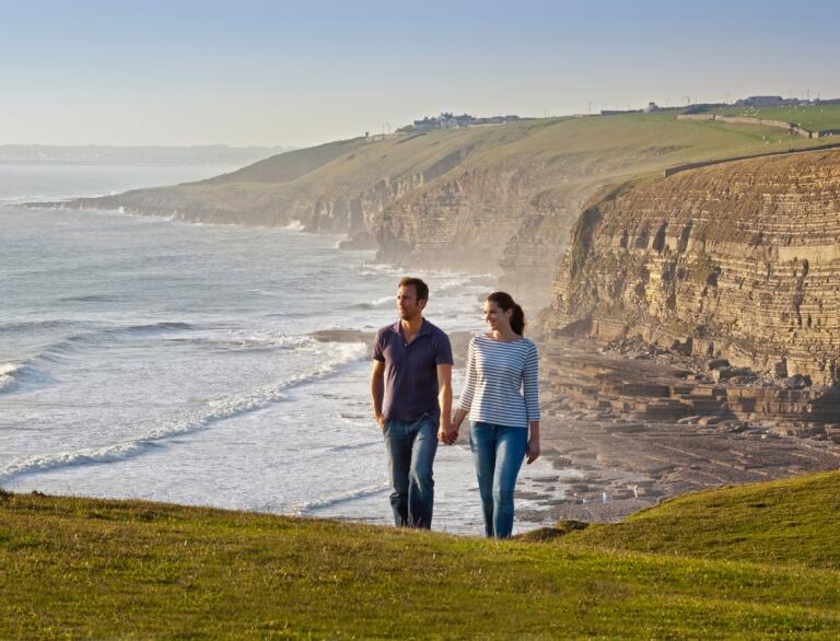 A couple walking on a coastal path with jurassic cliffs beyond.