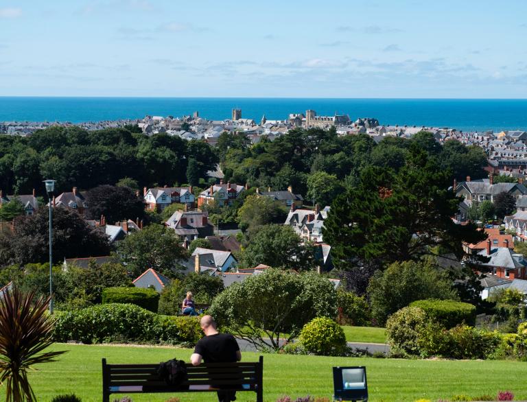 man on bench with view of Aberystwyth beyond.
