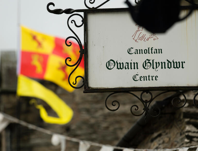 Owain Glyndŵr Centre sign, with the Owain Glyndŵr flag waving in the background.