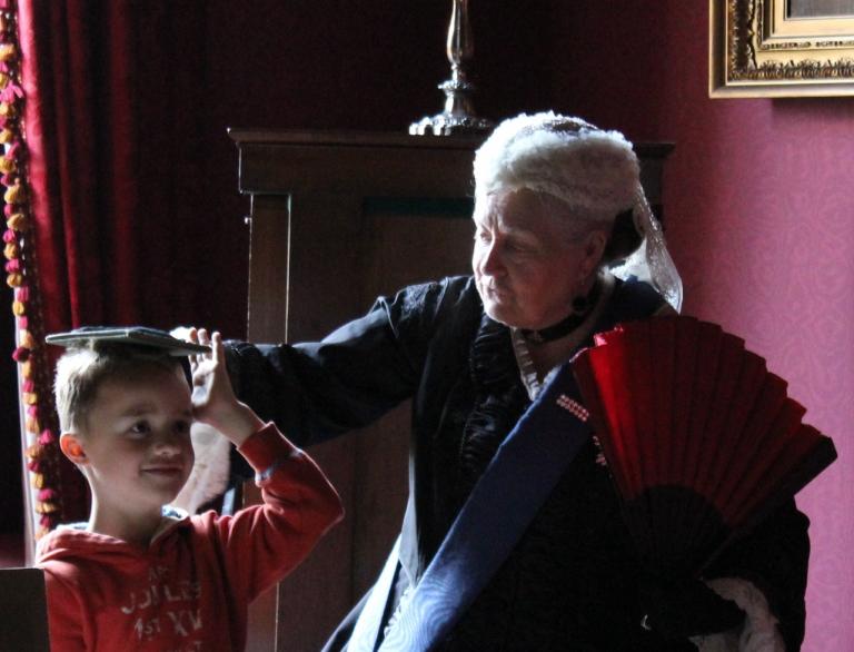 woman dressed in Victoria costume measuring height of boy
