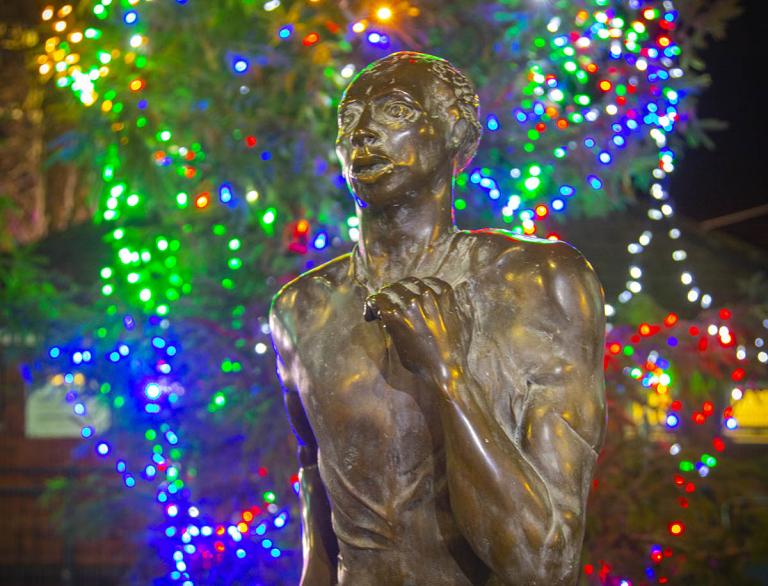 statue of man running with multi coloured strings of lights in background.