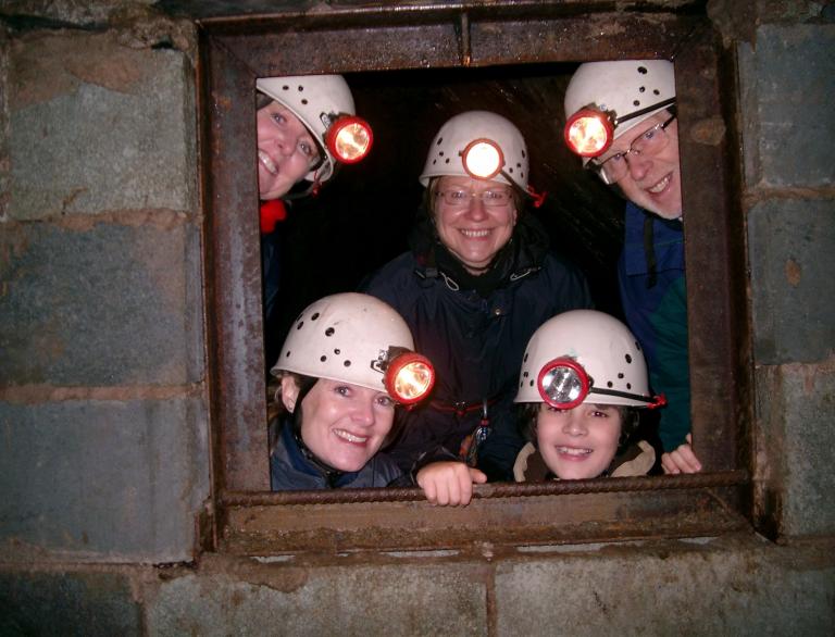 Family with hard hats with lights smiling and looking through the hatch in mine