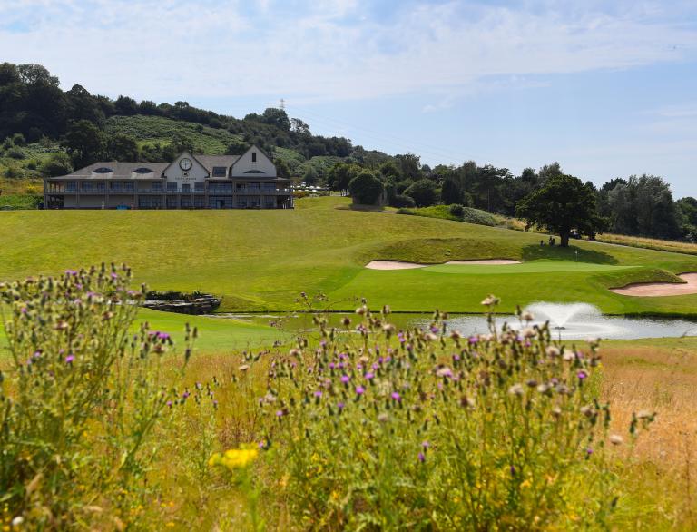 golf course with wild flowers in foreground and lake and bunkers plus building in background