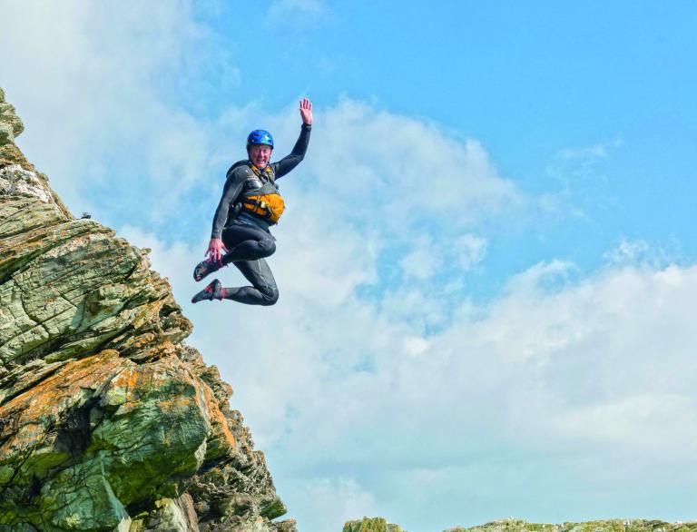 Man jumping from a rock into the sea while coasteering.