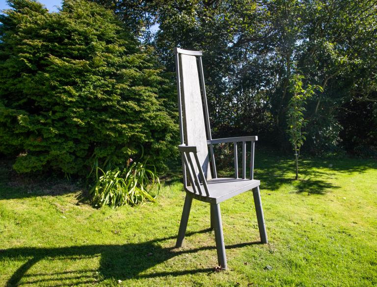 An art installation in the form of a large wooden stick chair in a garden