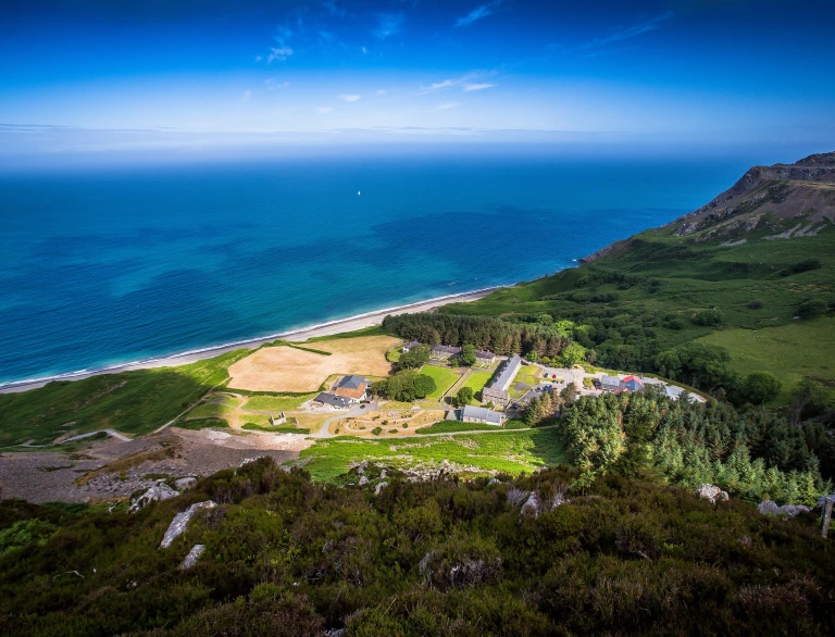 Aerial shot of Nant Gwrtheyrn surrounded by green landscape and the sea.