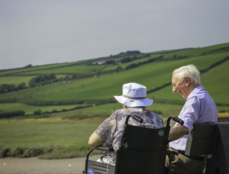 Senior couple female wheelchair user and male enjoying view out to sea.