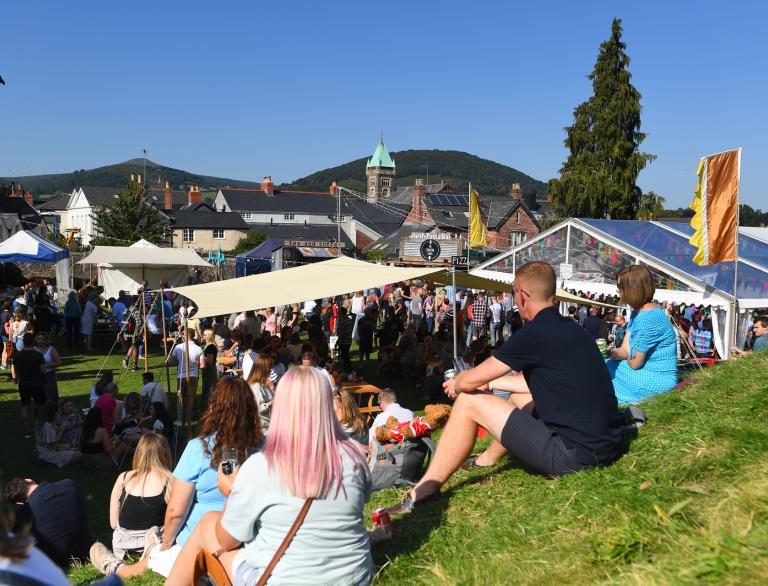 People sat on grass enjoying food at a festival.