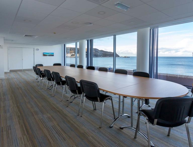Boardroom desk with chairs around looking out of the floor to ceiling windows onto the sea and promenade. 