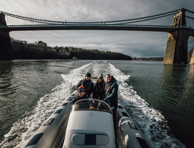 Four people on a boat ride with the Menai Bridge behind them