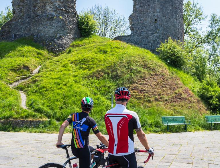 Two cyclists in front of a ruined castle tower.
