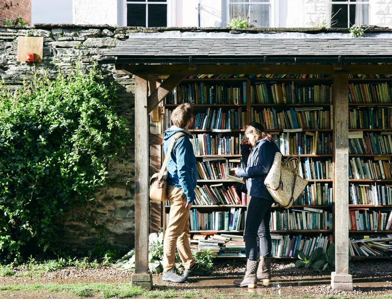 Zwei Personen sehen sich Bücher in einem im Freien stehenden Bücherregal an.