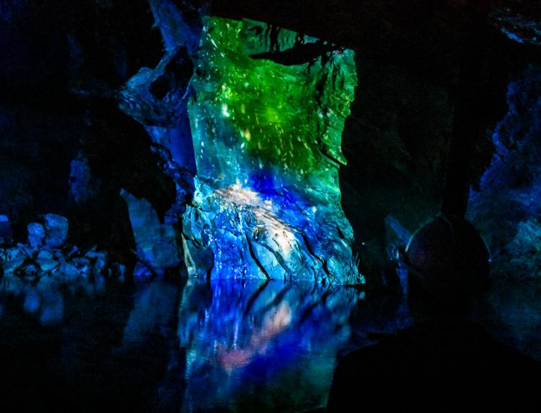 Slate rocks in an underground cavern lit up in colour, reflecting in the water.
