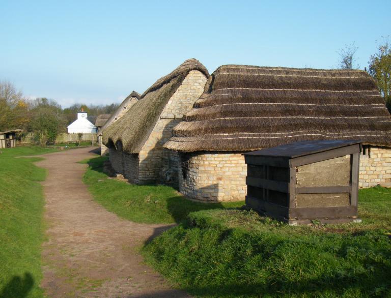Thatched stone buildings  with shadow of gate in foreground.