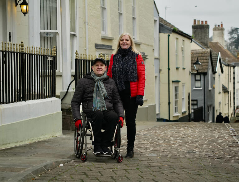 A man using a wheelchair and a woman in a narrow street.
