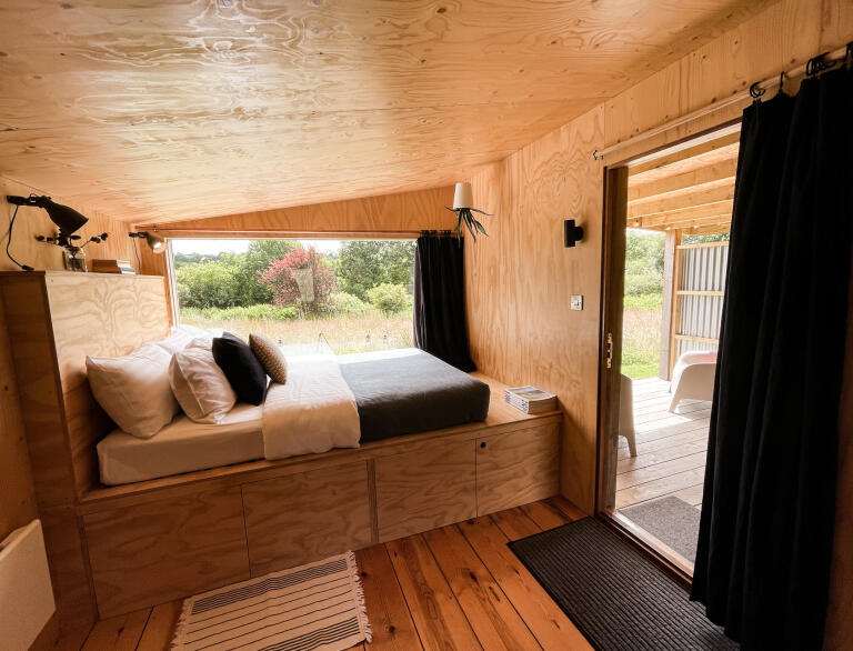 Innenansicht einer Holzhütte mit Bett und großen Fenstern.