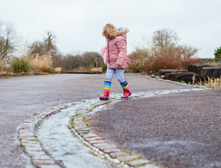 A small girl in wellies walking along a shallow winding stream.