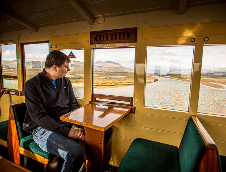 A man in a heritage railway carriage looking out over an estuary.