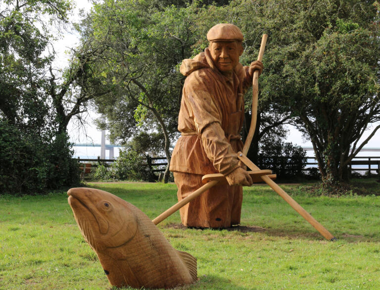 A large wooden sculpture of a man using a net to catch a fish.