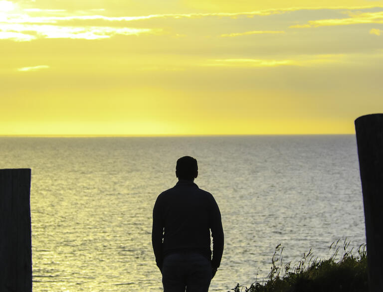 A silhouetted man watching a sunset over the sea.