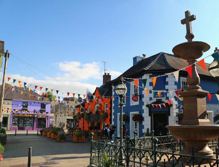 A town square with brightly painted buildings, bunting, and a marble fountain.