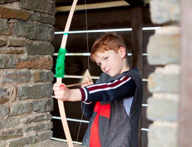 A young boy with a pretend bow and arrow in a castle.