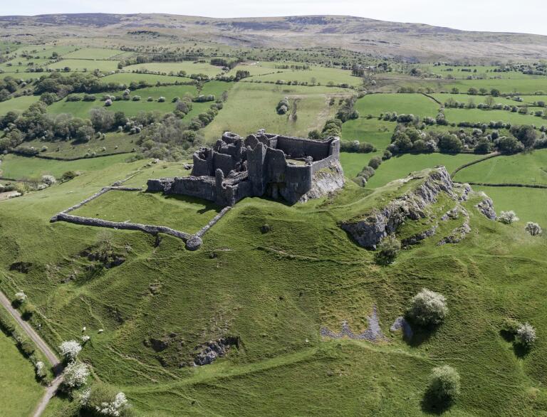 A ruined castle in green countryside from above.
