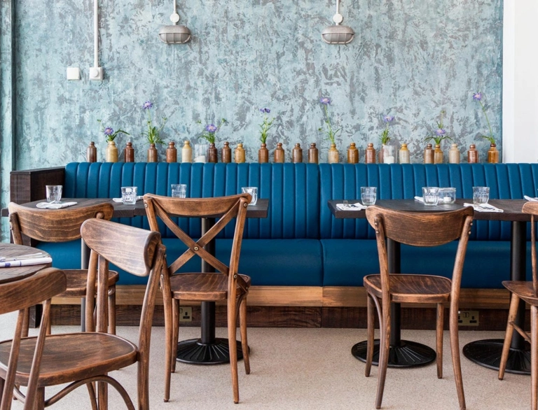 Einrichtung in einem Restaurant mit Holzstühlen, Tischen und einer blauen Bank.