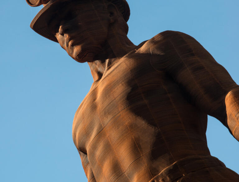 A weathered metal sculpture of a man wearing a miner's hat.