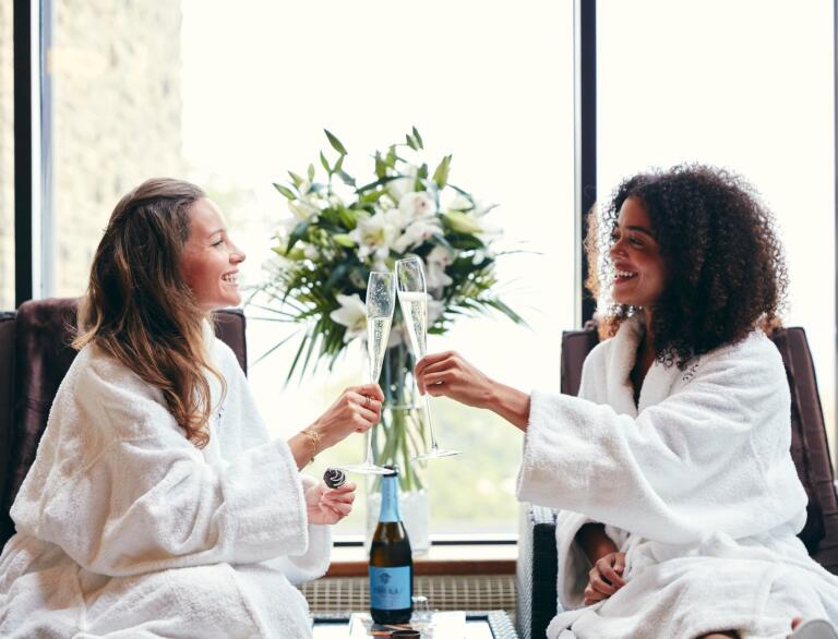 Two women enjoying a drink of bubbly in spa robes