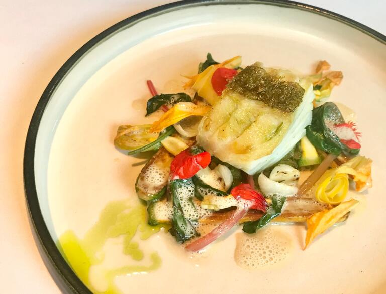 Ein Stück Fisch auf einem Bett aus gebratenem Gemüse, beträufelt mit einer grünen Soße.