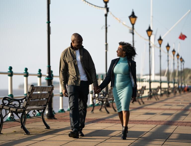 A man and a woman holding hands walking along a promenade.