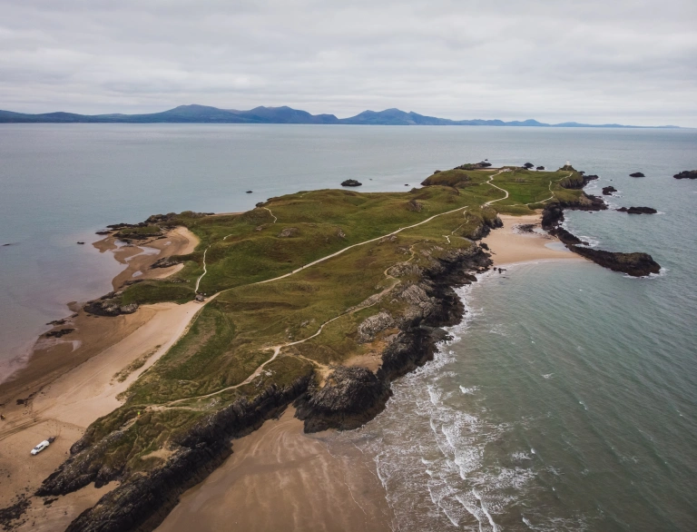 A grassy peninsula with golden beaches and a white lighthouse at the end.