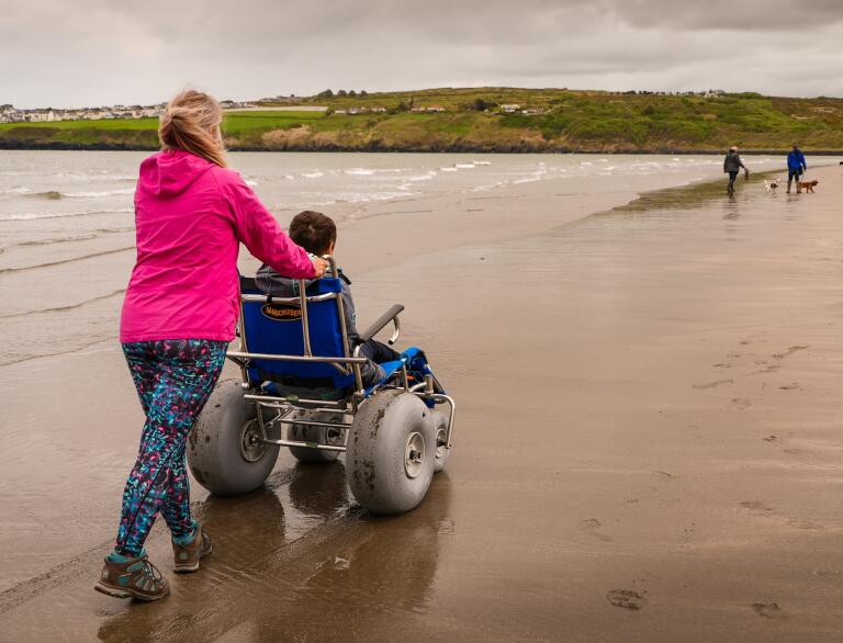 woman pushing someone in a beach wheelchair.
