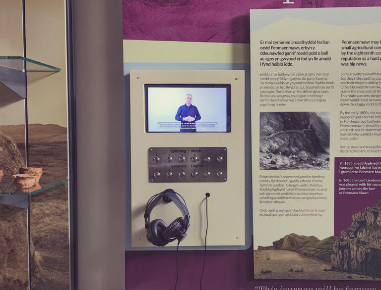 A museum display board in Welsh and English, with a British Sign Language interpretation screen.